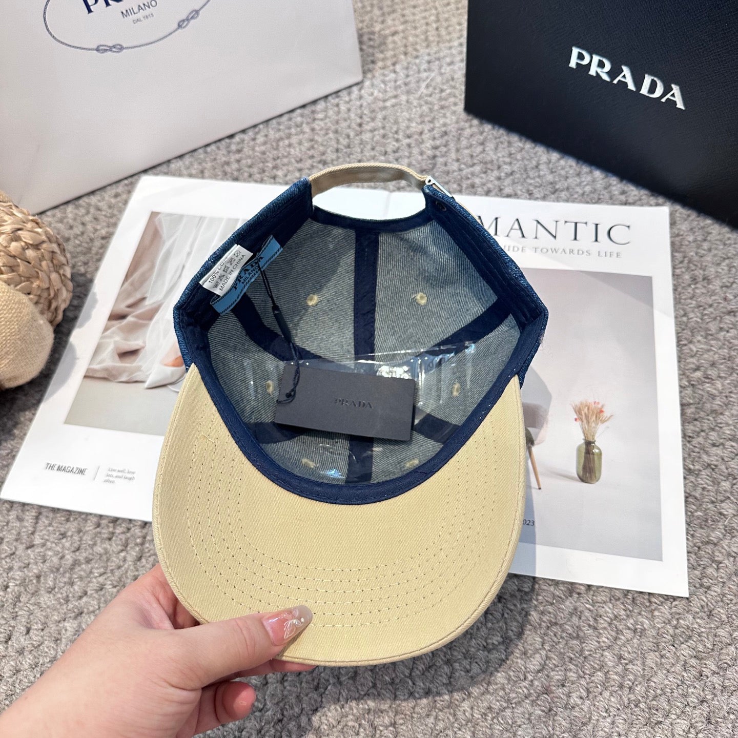 A two-tone baseball cap with a blue denim crown, beige brim, and a triangular metal logo badge.