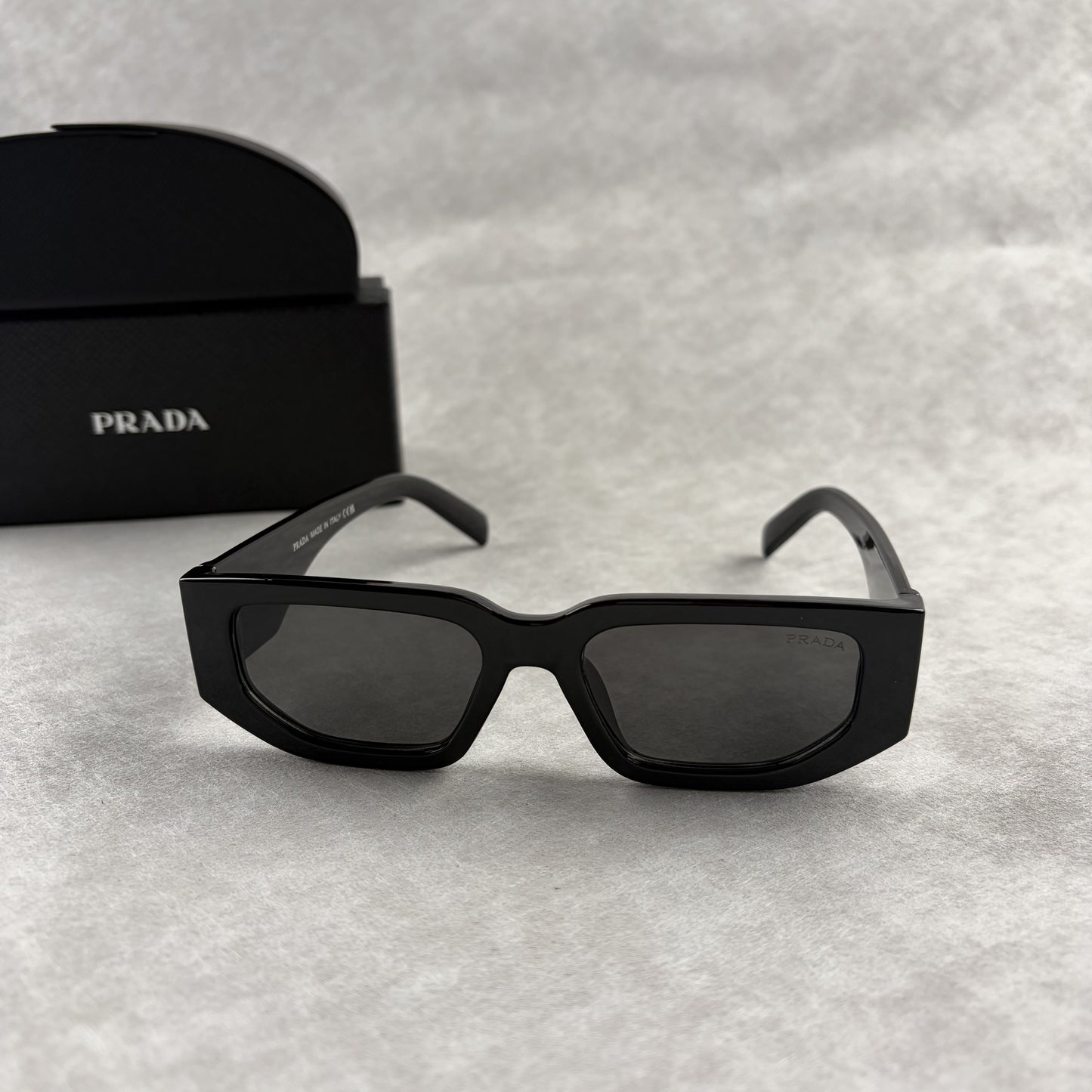 Modern black rectangular sunglasses with dark lenses and thick frame, isolated on a light background