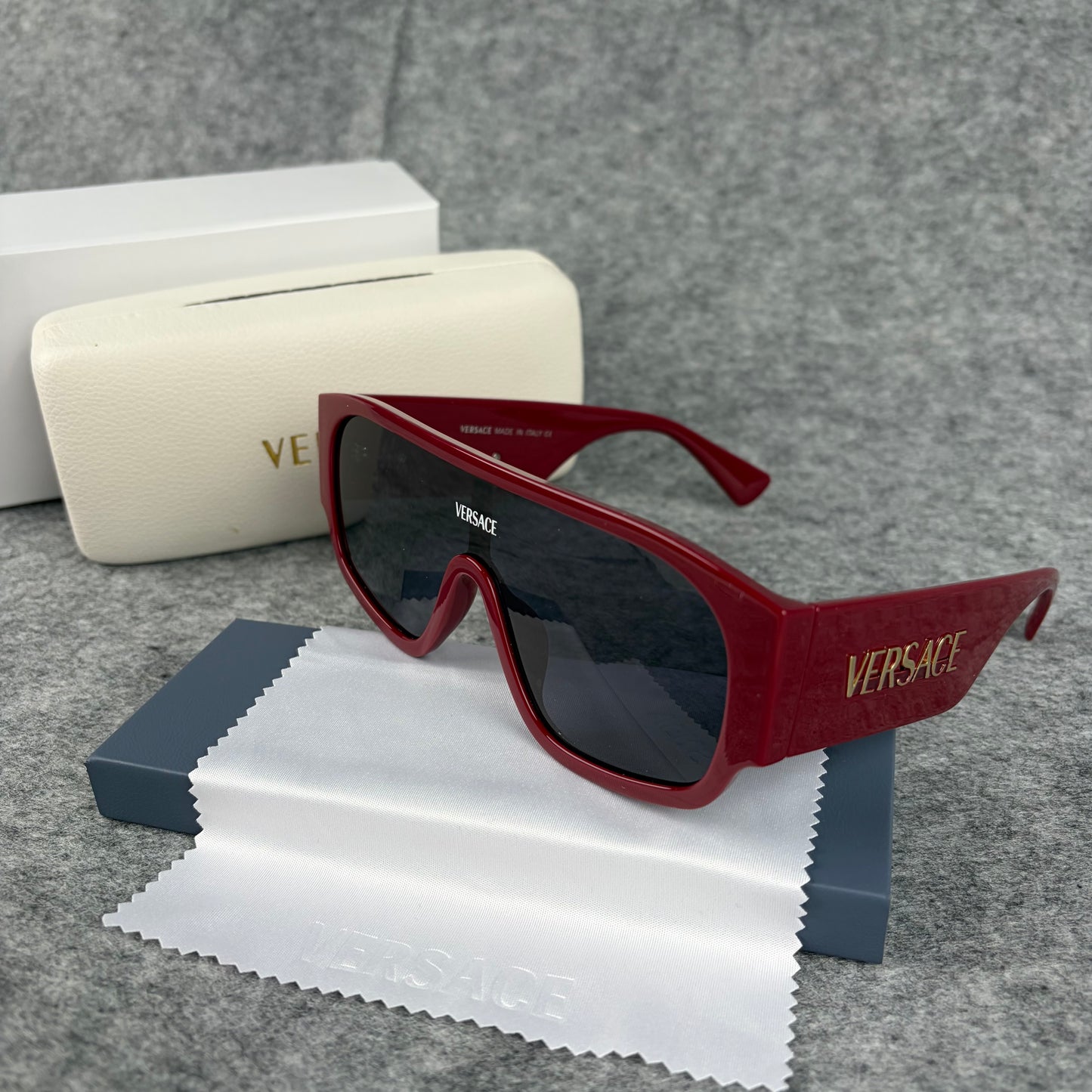 Oversized bold red shield sunglasses with dark lenses on a grey background with a white case.