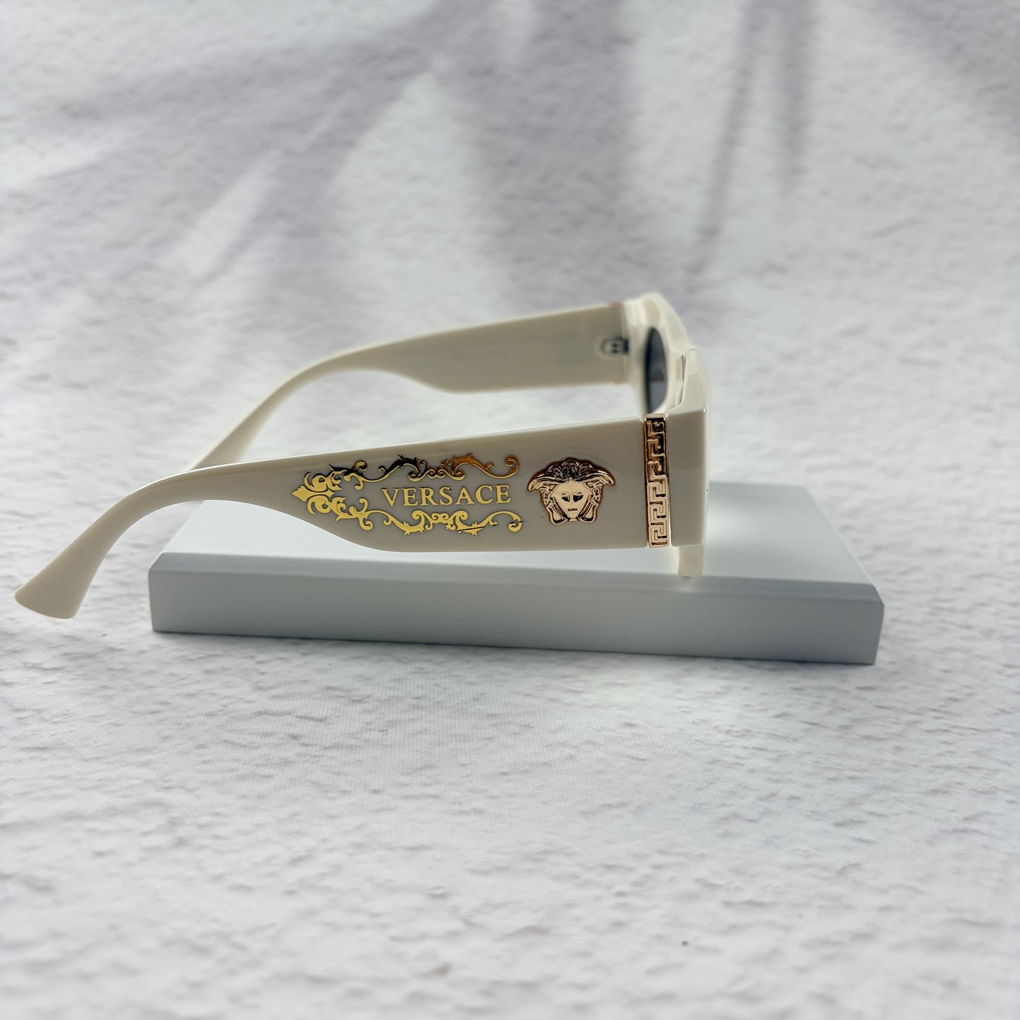 Off-white geometric cat-eye sunglasses with gold metal side accents, resting on a white stand.
