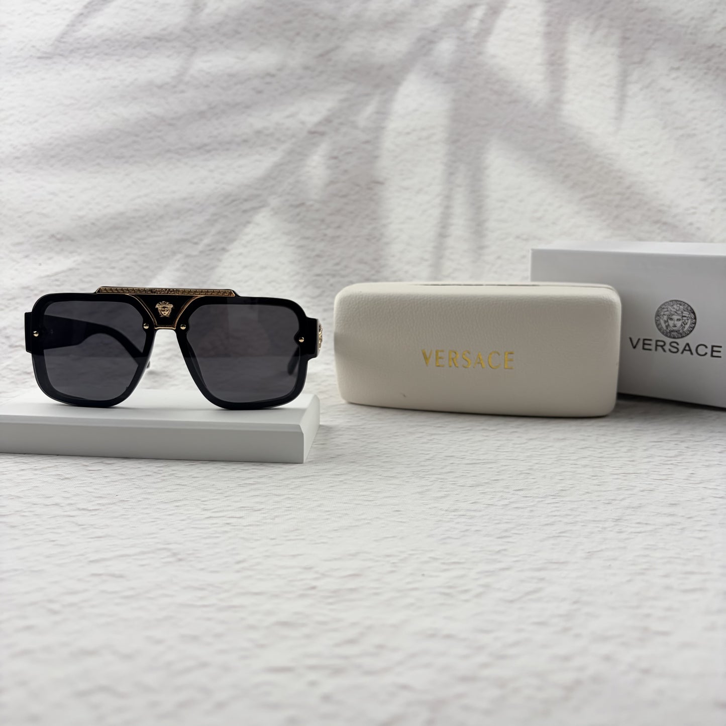 Oversized black flat-top sunglasses with a gold metal bridge and gold emblems on the temples.