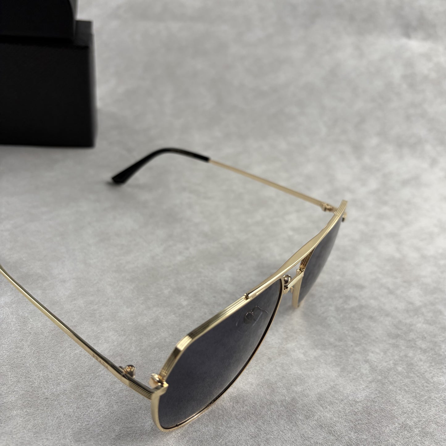 A pair of gold metal aviator sunglasses with dark lenses resting on a light grey textured background
