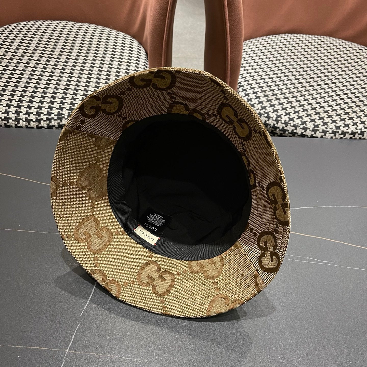 A beige canvas bucket hat with an all-over brown monogram pattern and a decorative gold-toned emblem