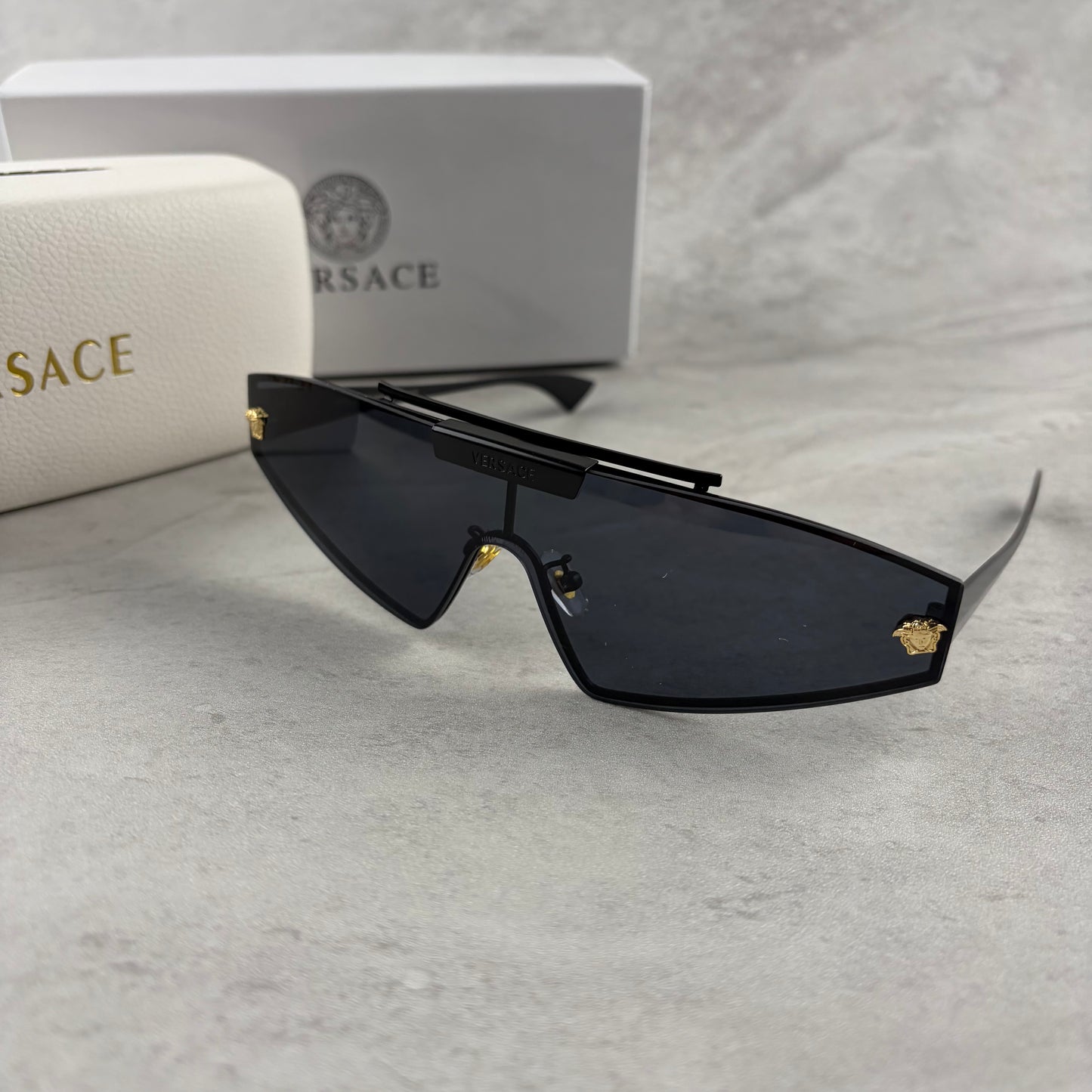 Modern shield sunglasses with a sleek black frame and dark tinted lenses on a grey background.