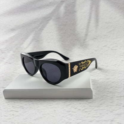 Black cat-eye sunglasses featuring gold-toned baroque temple embellishments on a white textured base