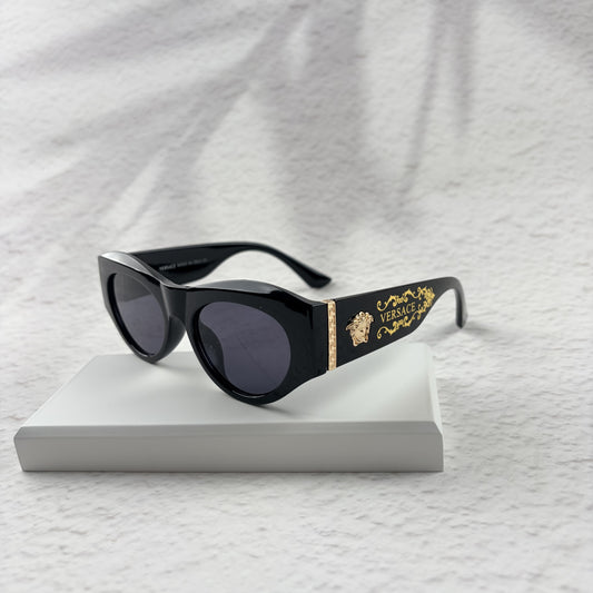 Black cat-eye sunglasses featuring gold-toned baroque temple embellishments on a white textured base