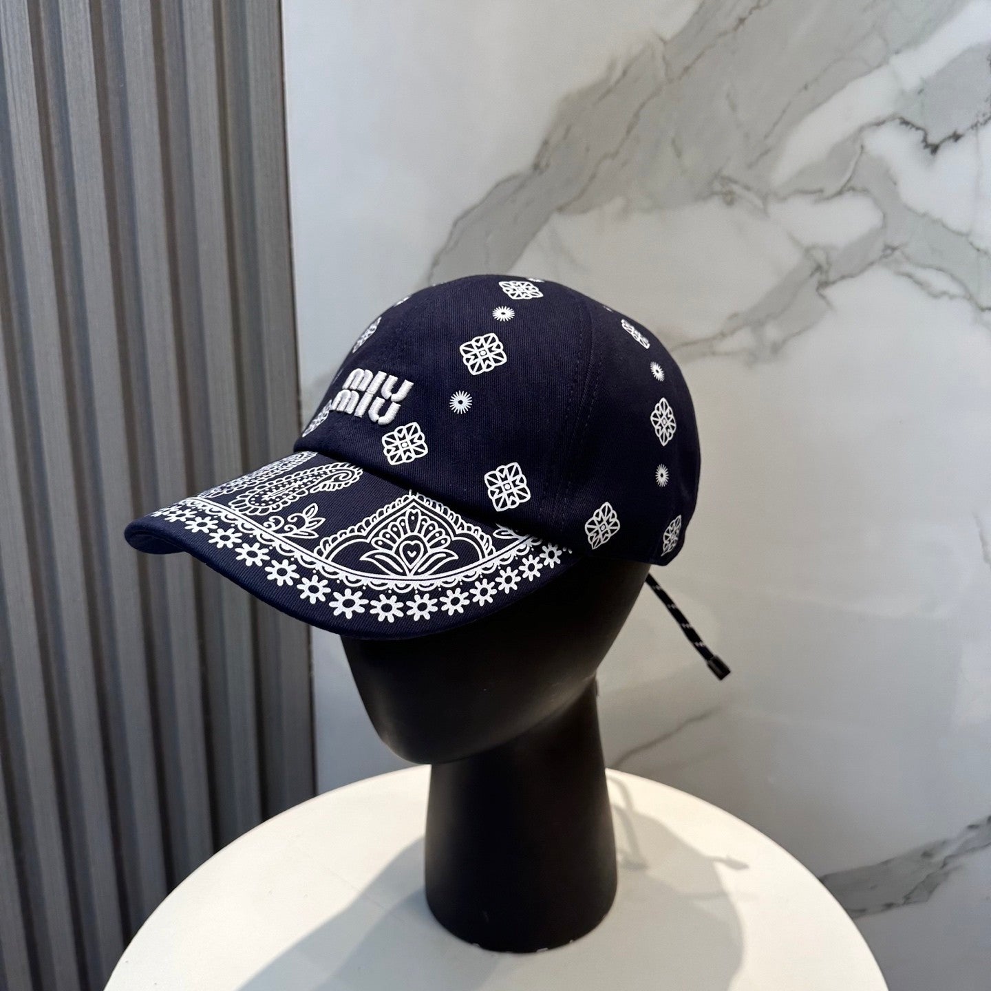 Navy blue baseball cap with white embroidered paisley patterns and an adjustable back strap.