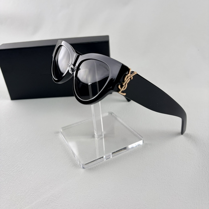 A pair of black cat-eye sunglasses with gold-tone hardware on the temples, displayed on a stand.