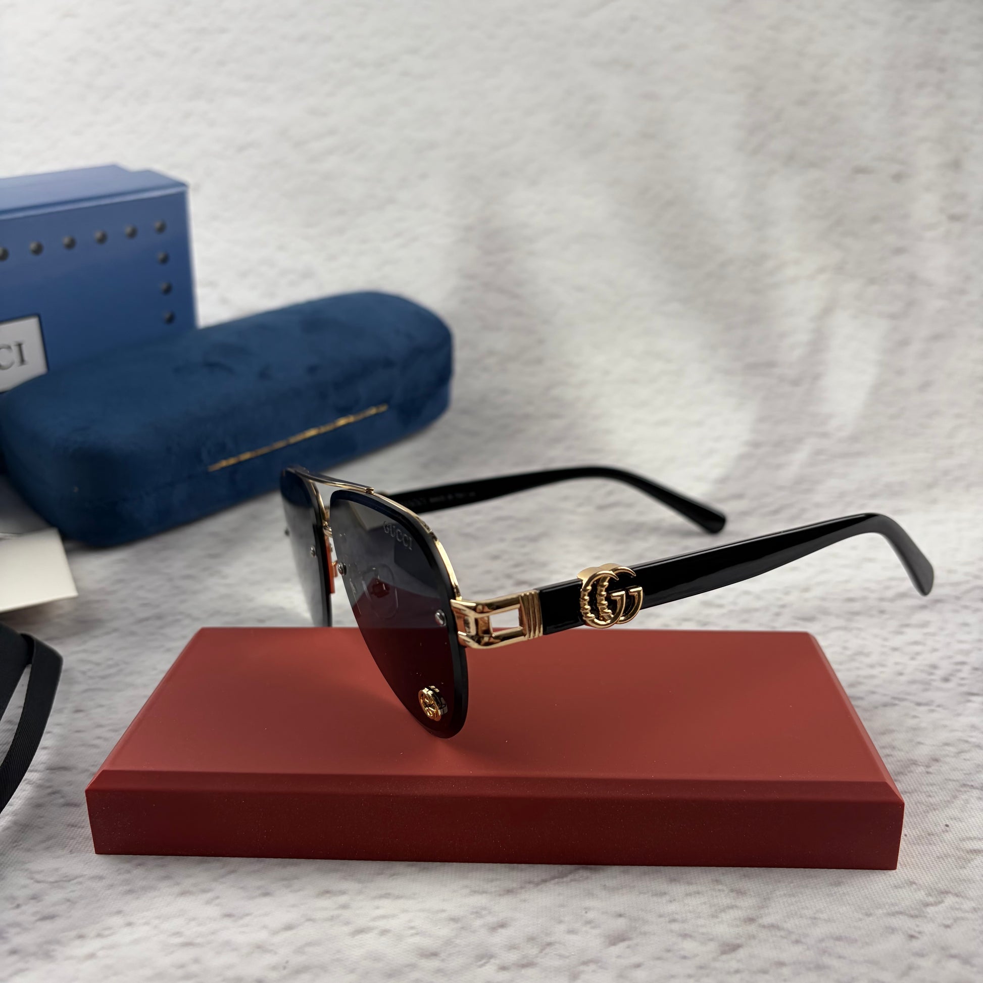 Pilot sunglasses with gold frame accents and dark lenses on a red display case.