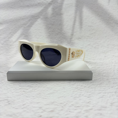 Off-white geometric cat-eye sunglasses with gold metal side accents, resting on a white stand.
