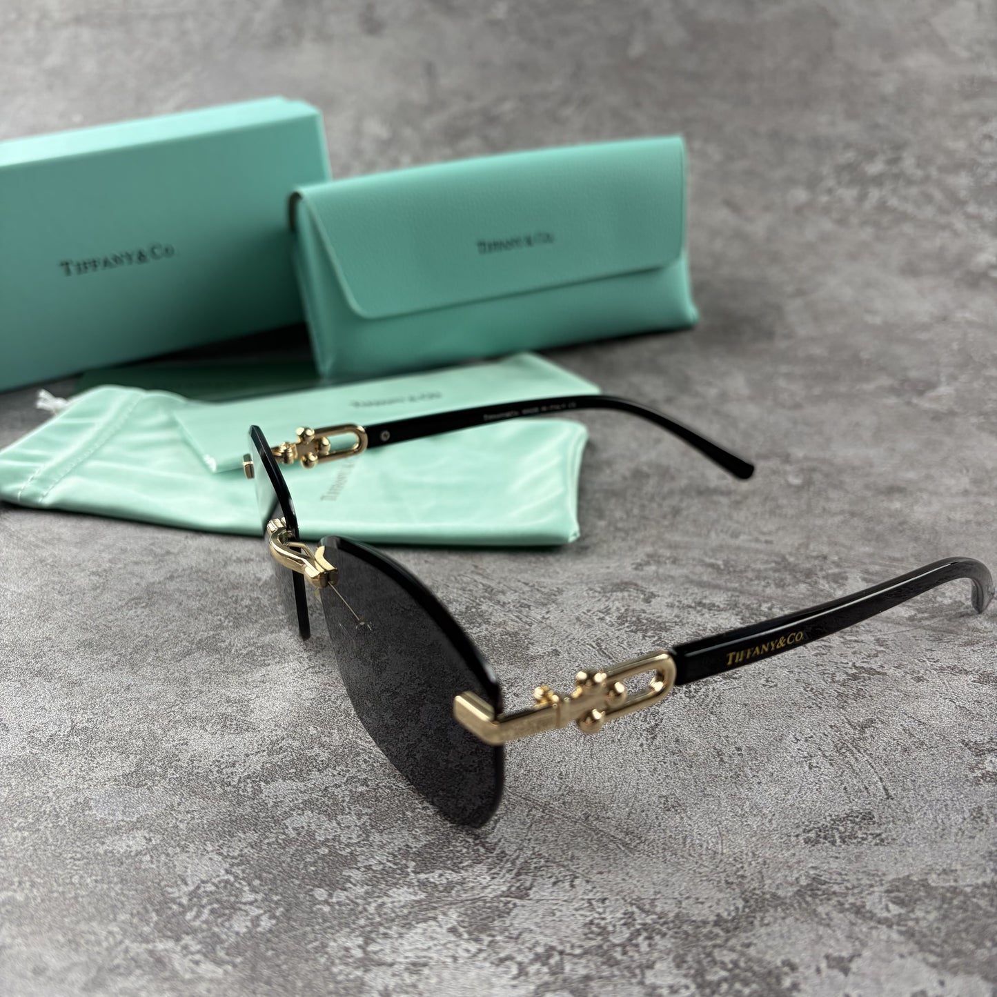 Rimless gradient sunglasses with gold-tone metal frames and black temple arms on a grey surface.