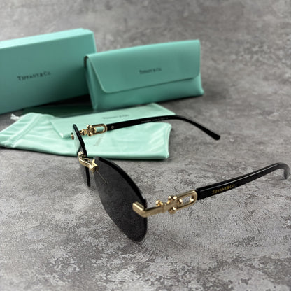 Rimless gradient sunglasses with gold-tone metal frames and black temple arms on a grey surface.