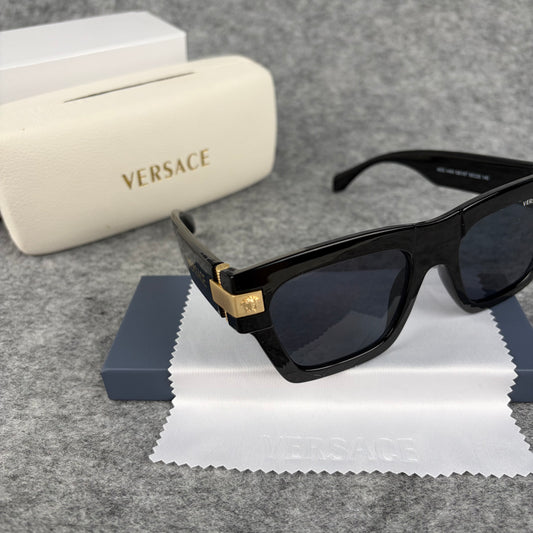 Black square-frame sunglasses with gold-tone metal temple accents, resting on a white cleaning cloth