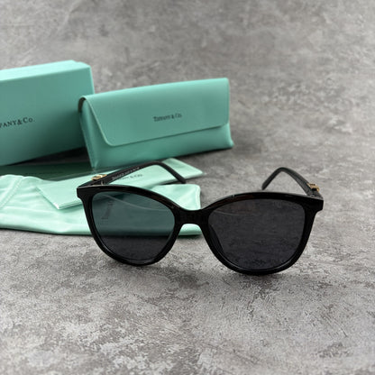 Black cat-eye sunglasses with decorative side temple accents, presented with a branded protective ca