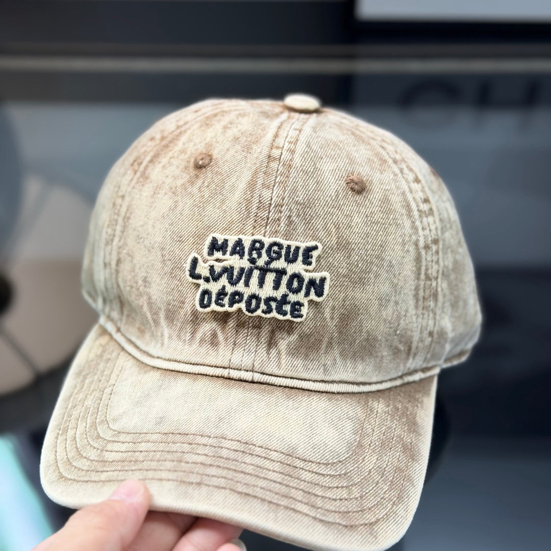 Vintage style distressed light brown denim baseball cap with embroidered letter patch on front.
