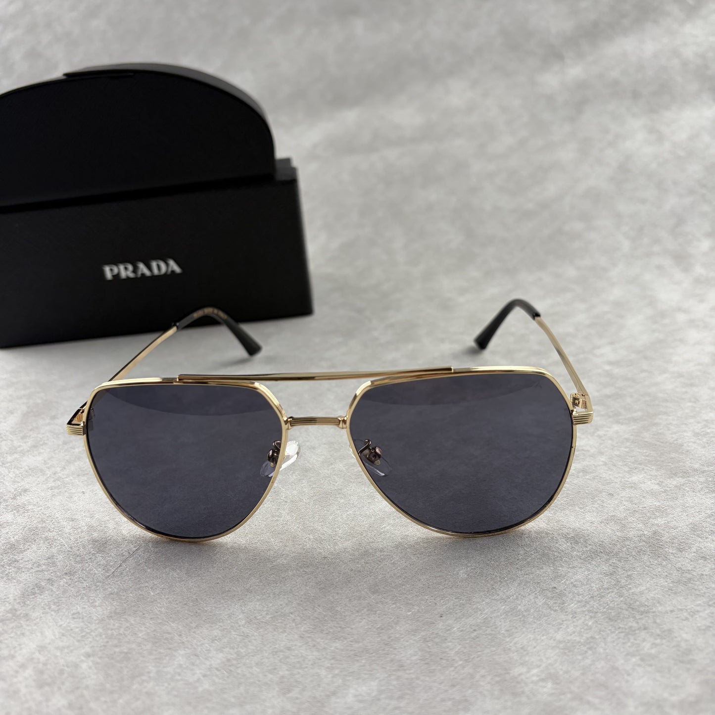 A pair of gold metal aviator sunglasses with dark lenses resting on a light grey textured background