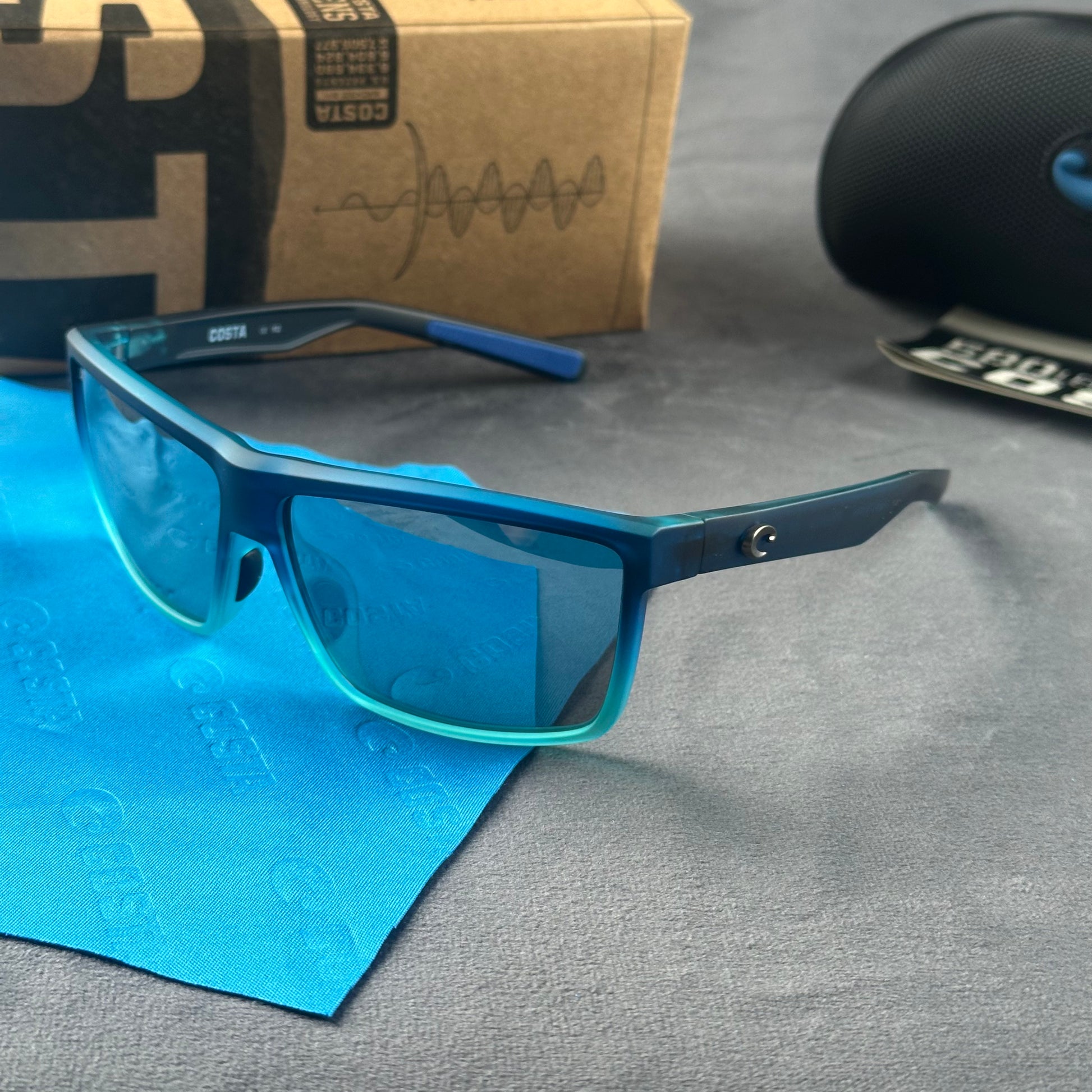 Blue and teal gradient frame sport sunglasses with polarized lenses resting on a blue cloth.