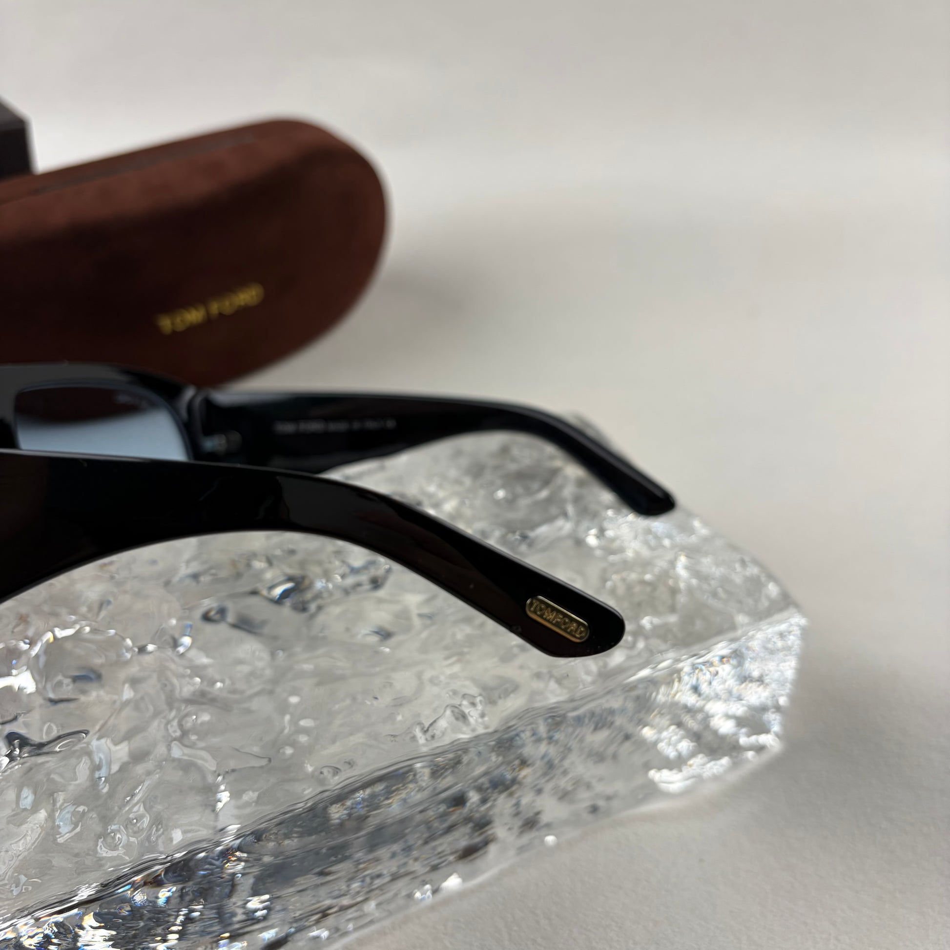 Black acetate oversized aviator sunglasses with blue tinted lenses resting on a clear ice-like block
