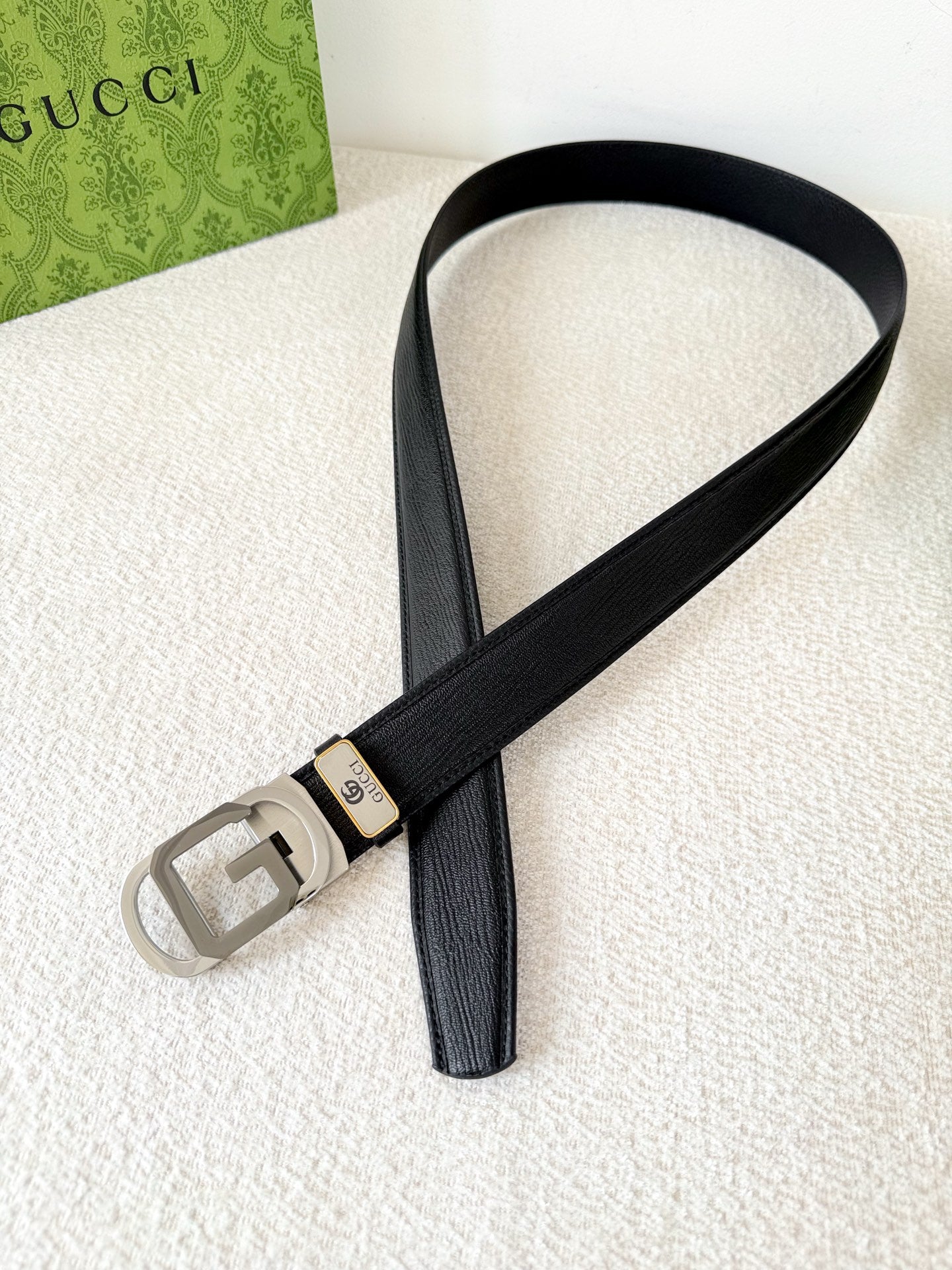 Black textured genuine leather belt with a modern metallic geometric buckle on a white surface.