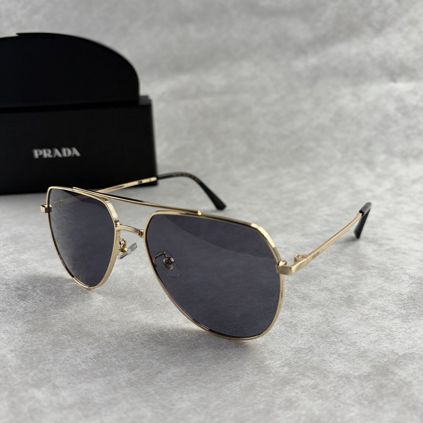 A pair of gold metal aviator sunglasses with dark lenses resting on a light grey textured background