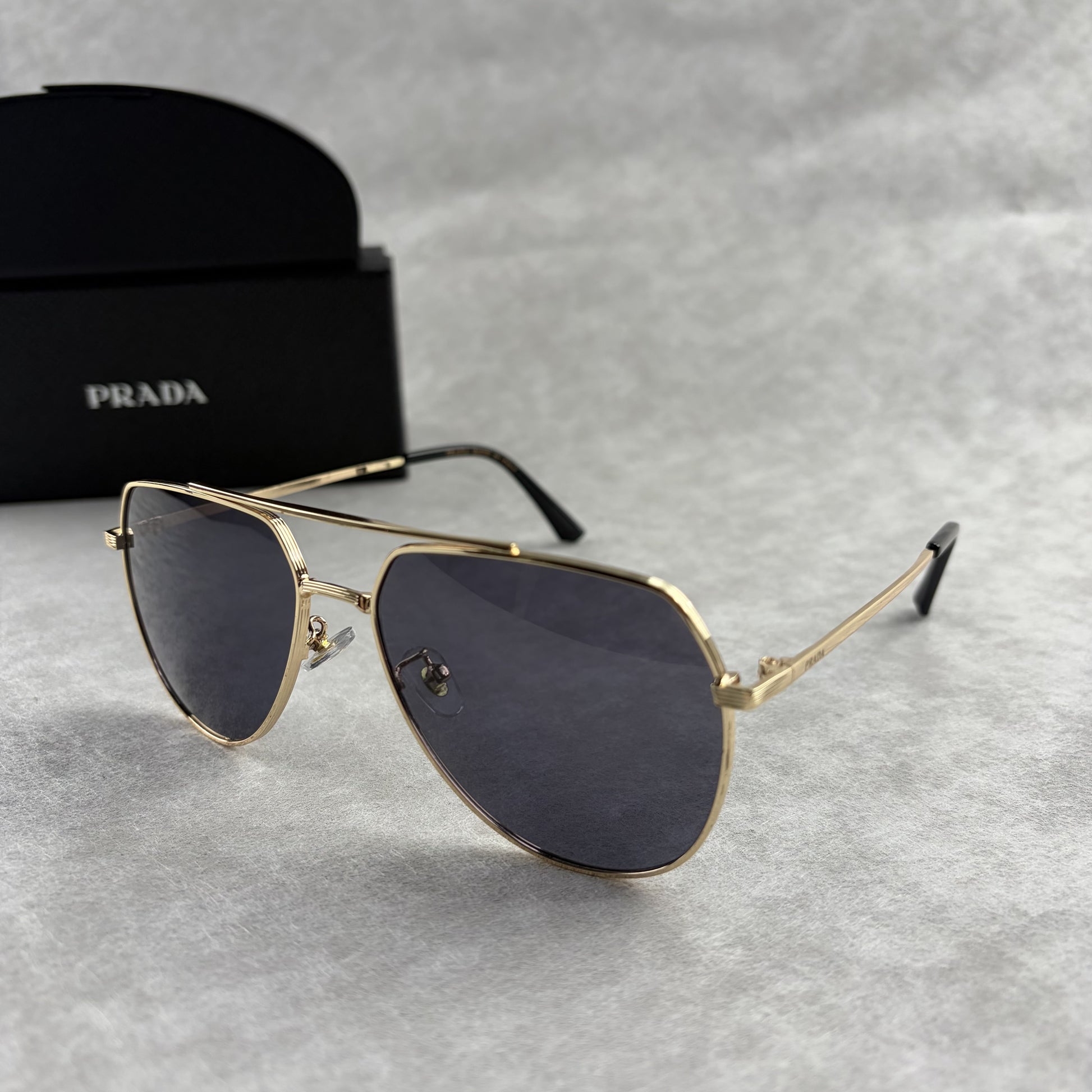 A pair of gold metal aviator sunglasses with dark lenses resting on a light grey textured background