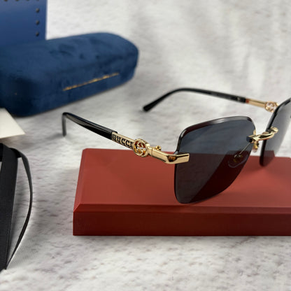 Rimless rectangular sunglasses with gold-tone metal arms and dark lenses on a red display stand.