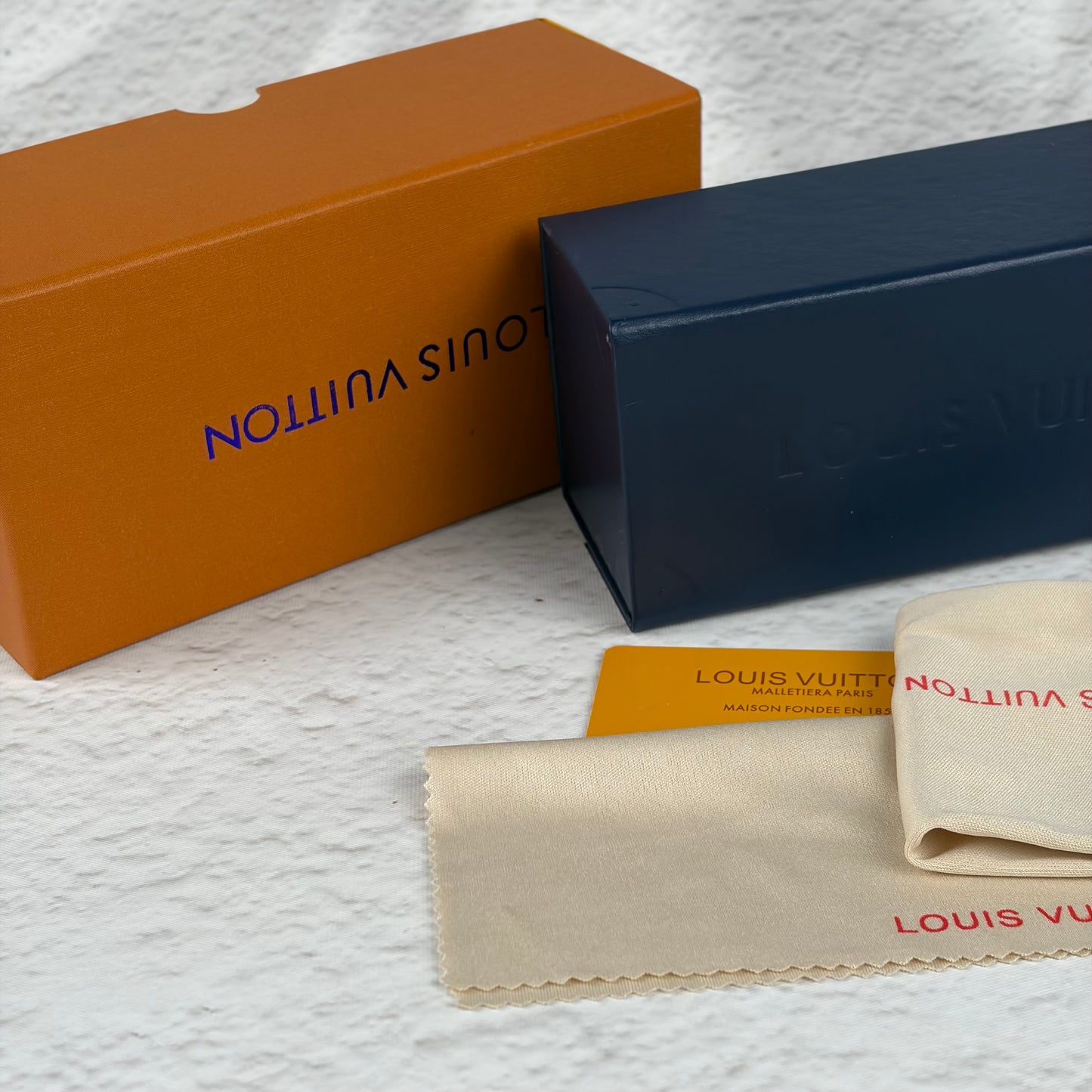 Rimless sunglasses with gold metal arms and dark gradient lenses resting on a white display block.