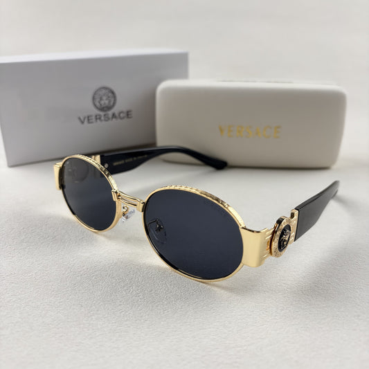 Oval gold metal frame sunglasses with black temples and dark tinted lenses, shown with a storage cas