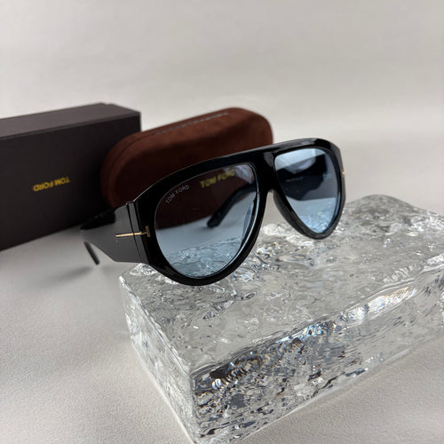 Black acetate oversized aviator sunglasses with blue tinted lenses resting on a clear ice-like block