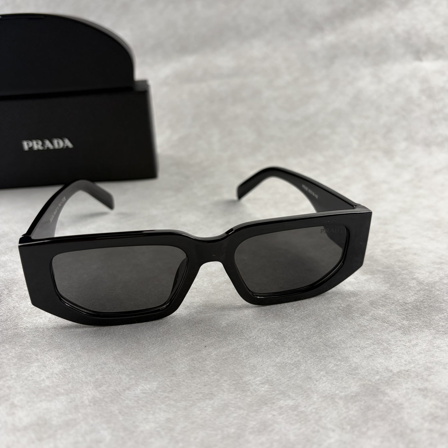 Modern black rectangular sunglasses with dark lenses and thick frame, isolated on a light background