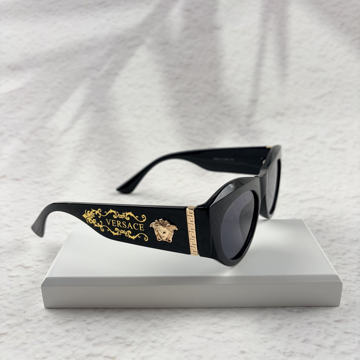 Black cat-eye sunglasses featuring gold-toned baroque temple embellishments on a white textured base