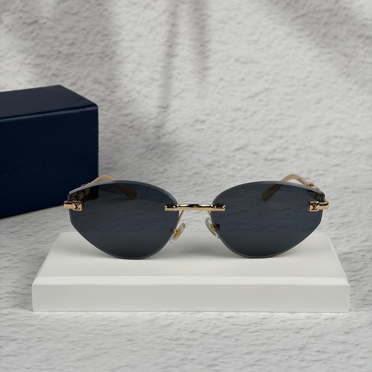 Rimless sunglasses with gold metal arms and dark gradient lenses resting on a white display block.