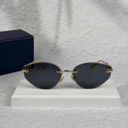 Rimless sunglasses with gold metal arms and dark gradient lenses resting on a white display block.