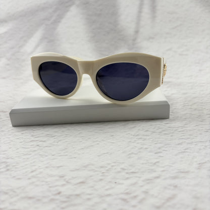 Off-white geometric cat-eye sunglasses with gold metal side accents, resting on a white stand.