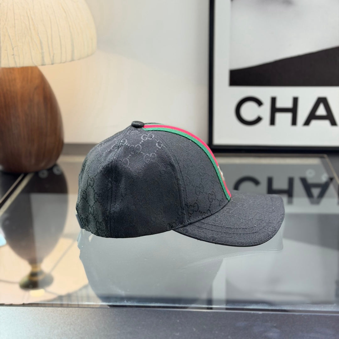 Close-up of a premium black baseball cap with a red and green center stripe and monogram pattern.