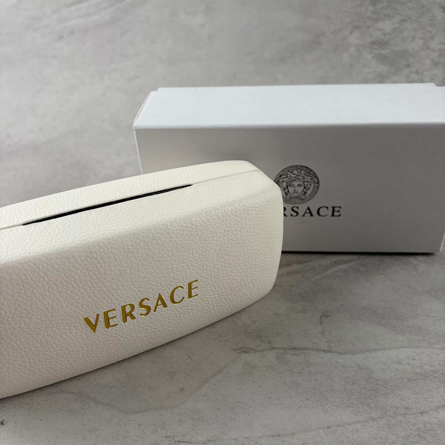 Oversized black shield sunglasses with gold metal accents on arms resting on a blue display box.
