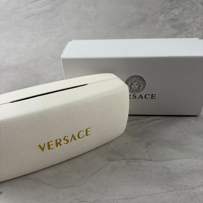 Oversized black shield sunglasses with gold metal accents on arms resting on a blue display box.