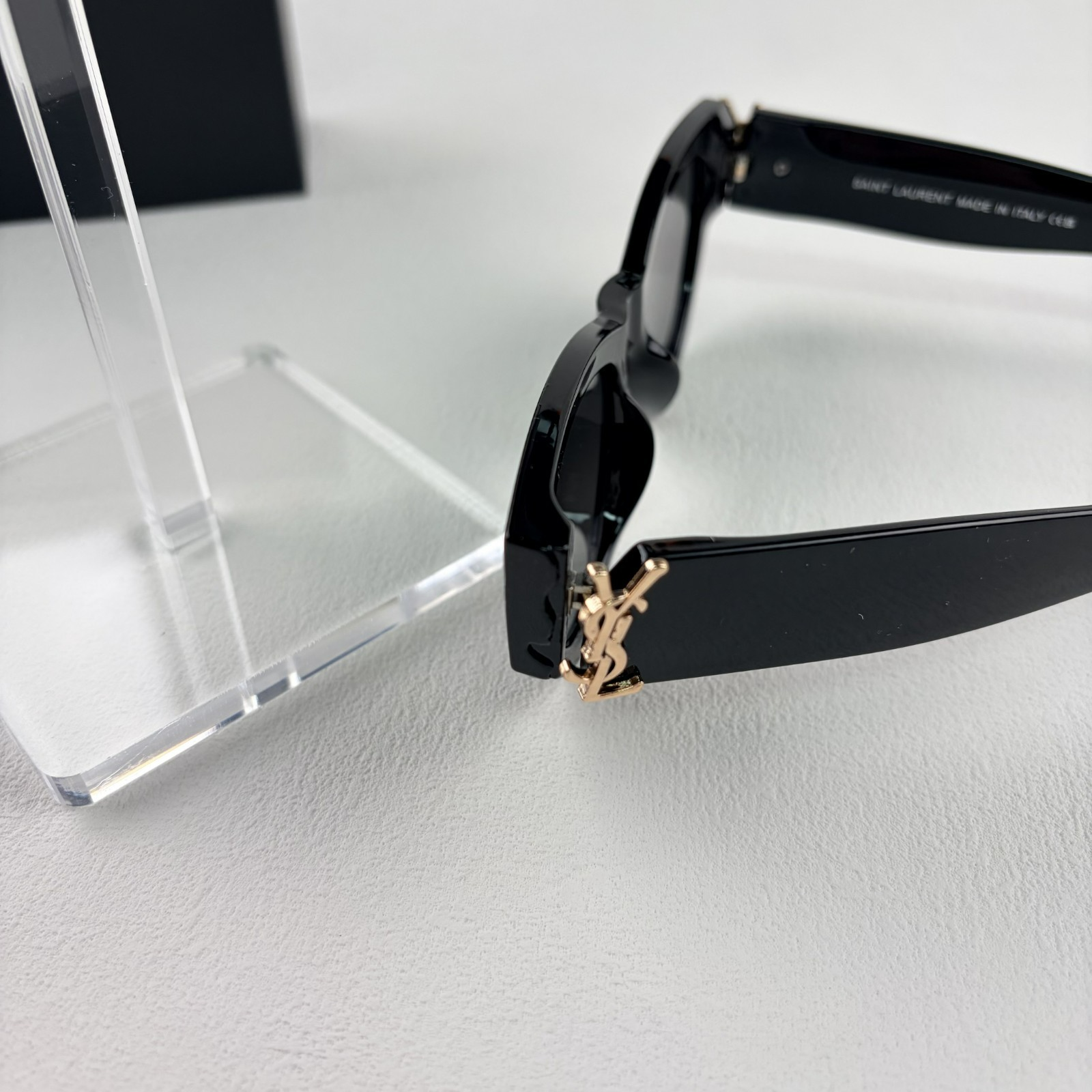A pair of black cat-eye sunglasses with gold-tone hardware on the temples, displayed on a stand.