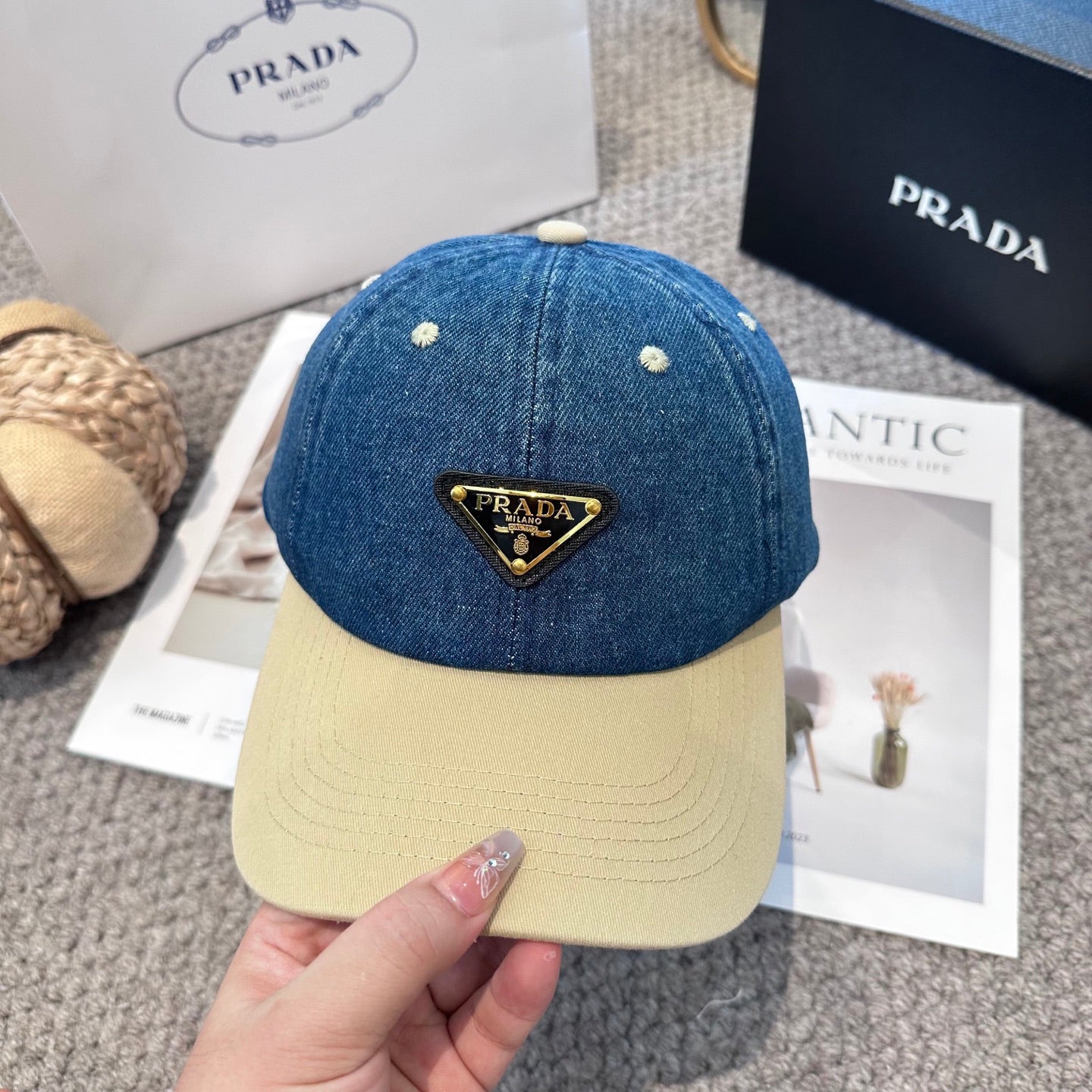 A two-tone baseball cap with a blue denim crown, beige brim, and a triangular metal logo badge.