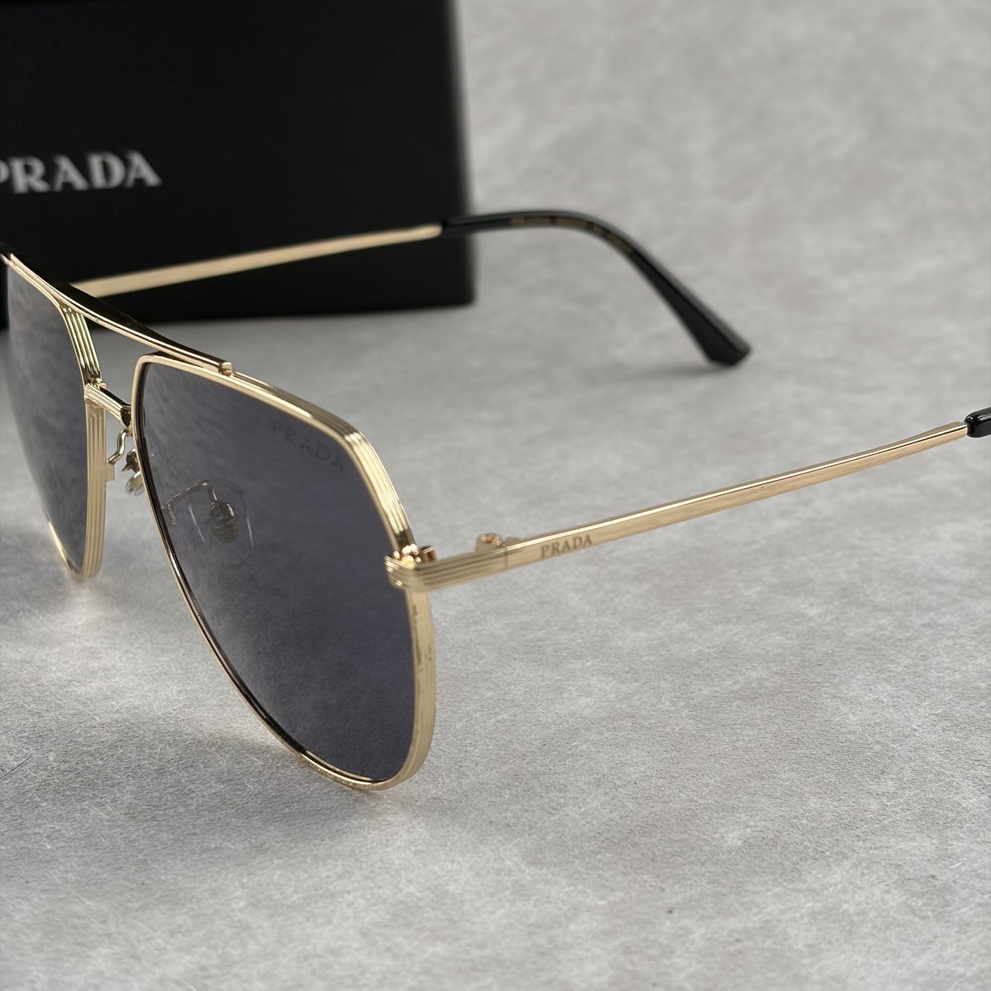 A pair of gold metal aviator sunglasses with dark lenses resting on a light grey textured background