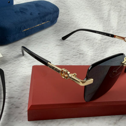 Rimless rectangular sunglasses with gold-tone metal arms and dark lenses on a red display stand.