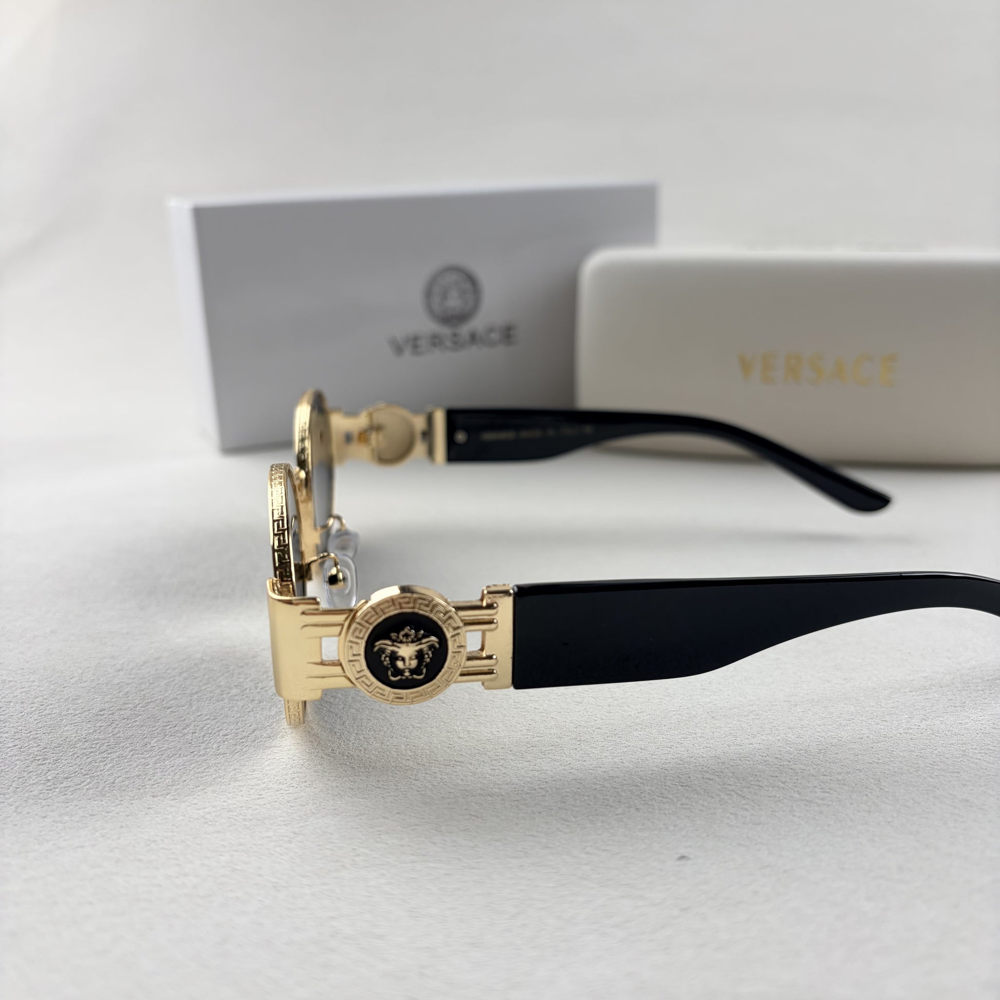 Oval gold metal frame sunglasses with black temples and dark tinted lenses, shown with a storage cas