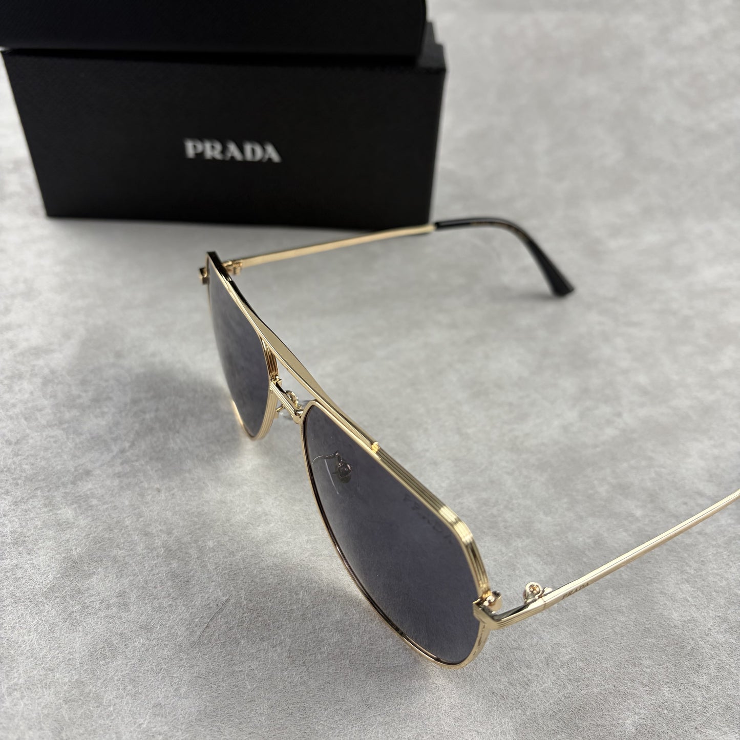 A pair of gold metal aviator sunglasses with dark lenses resting on a light grey textured background