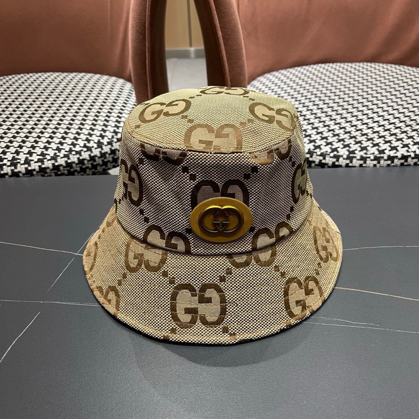 A beige canvas bucket hat with an all-over brown monogram pattern and a decorative gold-toned emblem