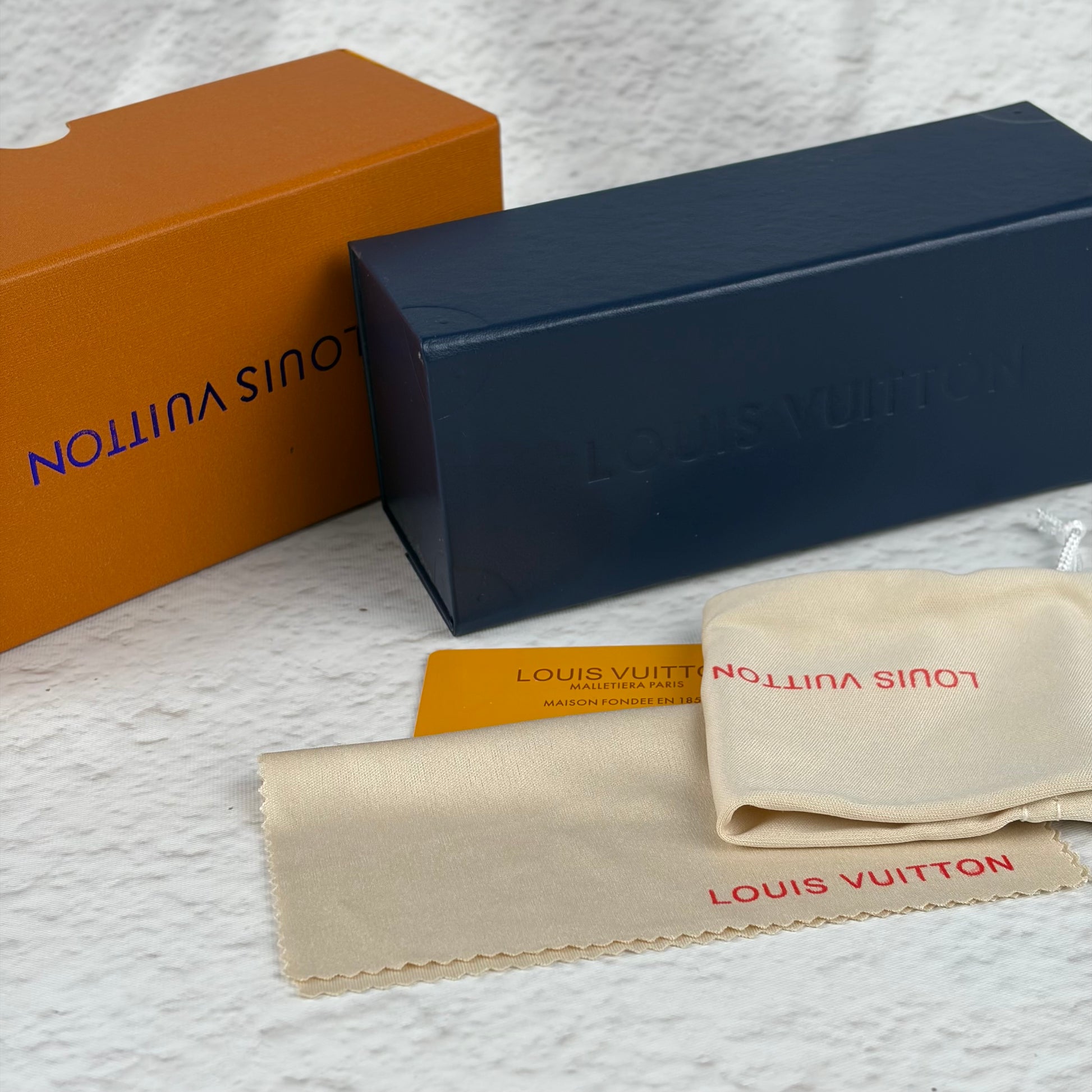 Rimless sunglasses with gold metal arms and dark gradient lenses resting on a white display block.