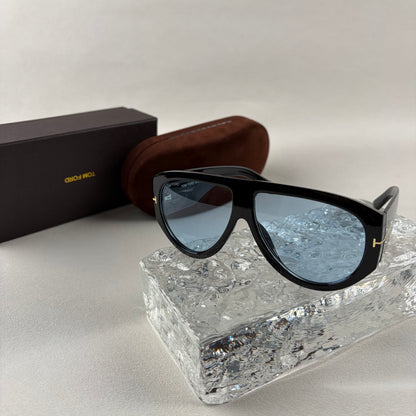 Black acetate oversized aviator sunglasses with blue tinted lenses resting on a clear ice-like block