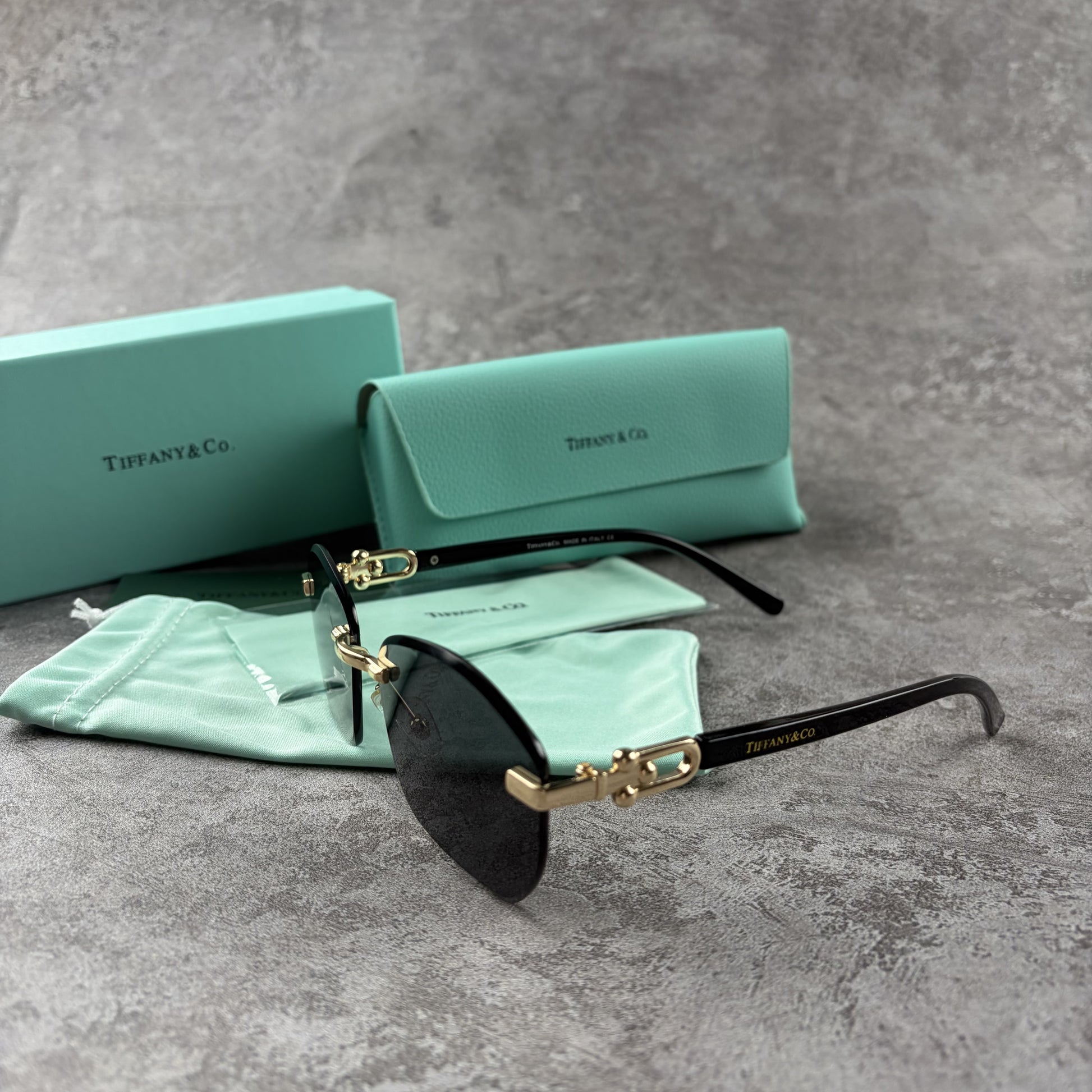 Rimless gradient sunglasses with gold-tone metal frames and black temple arms on a grey surface.