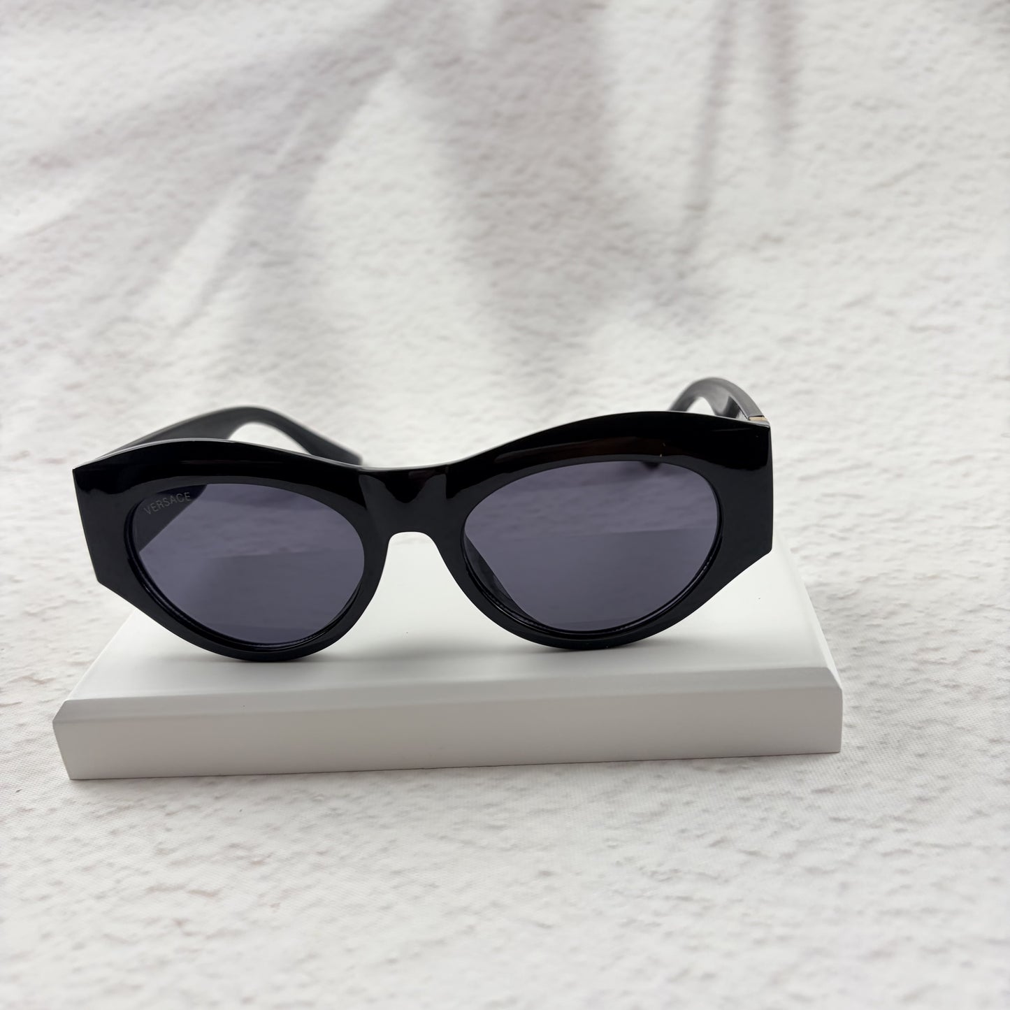 Black cat-eye sunglasses featuring gold-toned baroque temple embellishments on a white textured base