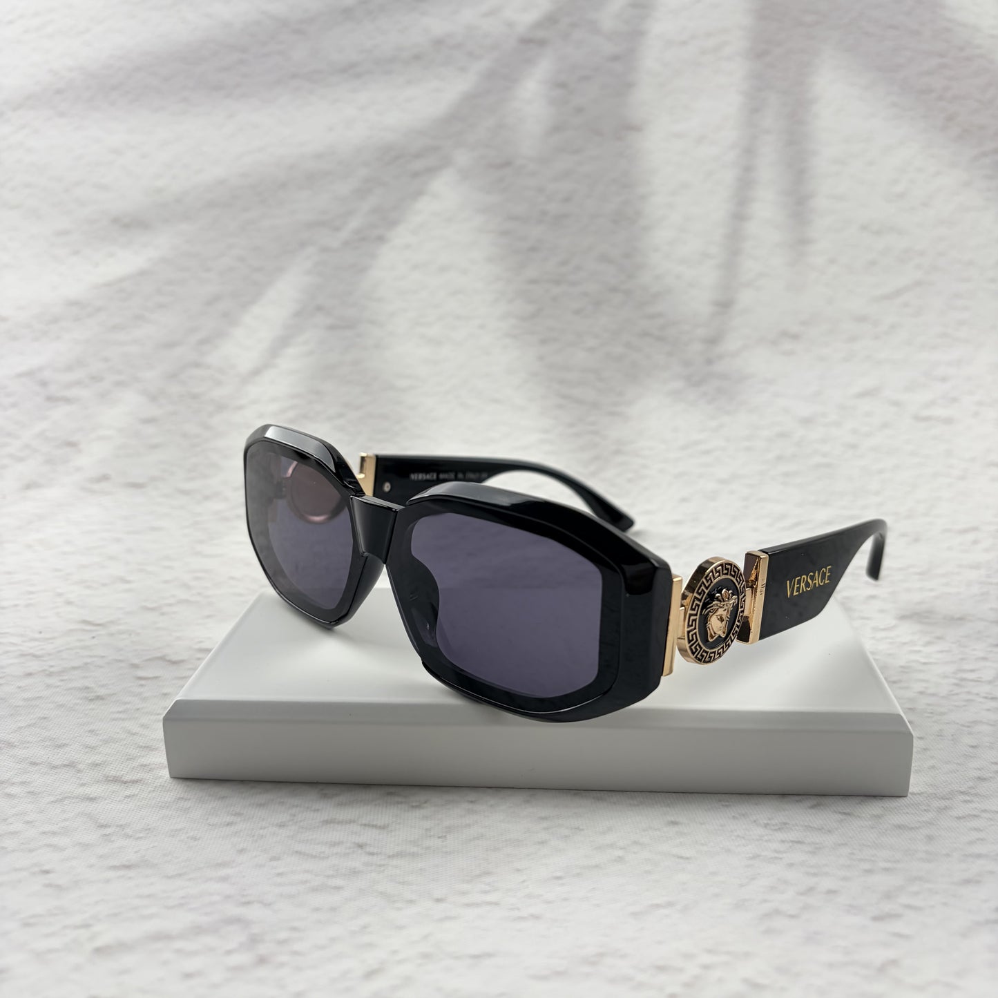 Black geometric sunglasses with gold side emblems resting on a white display block.