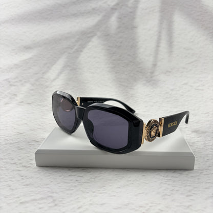 Black geometric sunglasses with gold side emblems resting on a white display block.